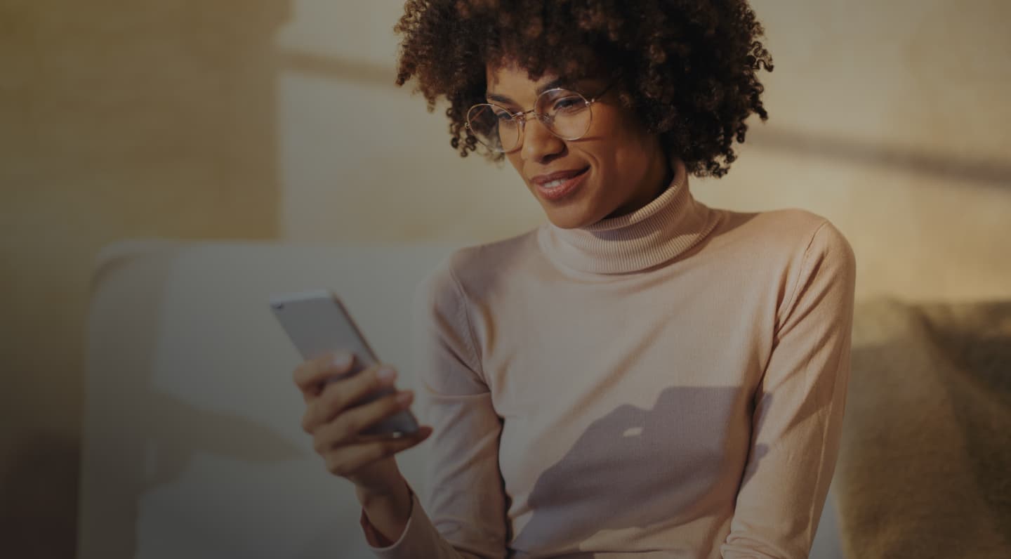 A woman sitting in sunlight smiling at her phone